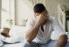Upset young man sitting in bed have problems with sex while his girlfriend sleep in bedroom in the morning